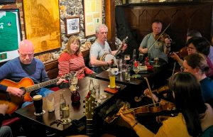 Large group of musicians sit in a traditional Irish pub playing Irish and contemporary instruments