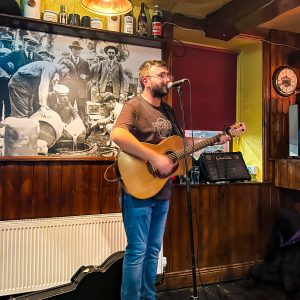 Man stands at microphone at Katie Dalys Heritage Pub & Kitchen with a guitar